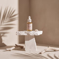 ROMERO SERUM de Nitiel sobre un pedestal de piedra, con sombras de palmera